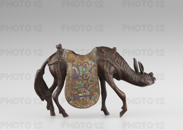 Sage on a Mule, cloisonné enamel, Qing 1644–1911, 19th century, China; sculpture depicting a sage riding a mule with men/figurines, mules, birds and zoomorphic motifs, plant motifs, scrolls, meander ornament; height 26.0 cm, width 25.5 cm, depth 6.0 cm., A small sculpted animal resembling a horse or donkey stands with its head lowered, rendered in brown metal with darker and lighter brown variations and areas of greenish patina. It wears a decorative saddle cloth that hangs down on both sides, showing a colorful painted or inlaid pattern with teal, blue, red, green, and gold tones against a gold-edged background. The animal has a detailed mane, visible harness straps, and a tail draped to one side; the surface shows wear and textured tooling. The background is a smooth gradient of light gray to white.