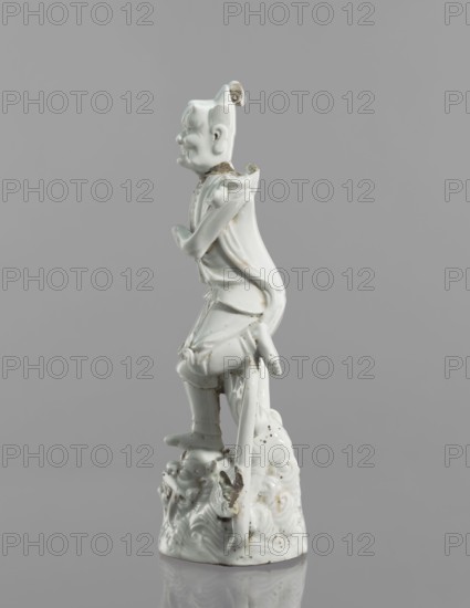 Kui Xing figurine with a leg resting on a mythical fish-dragon, ceramics, Chinese, 18th century, sculpture, height 29 cm; depiction of Kui Xing, dragons and ao mythology., A white glazed ceramic figurine of a standing person on a textured base, shown in profile facing left; the figure wears a flowing garment with draped folds and a long cape that extends behind, and has stylized hair or headwear with a small protrusion at the top; the figure’s arms are bent at the elbows with hands positioned near the chest and waist, and one leg is slightly raised with the foot resting on the ornate base; the base is textured with swirling, cloud-like forms and shows some rough, darker areas and chips; visible colors are white and small patches of darker brownish or grayish discoloration against a neutral gray background.