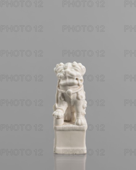 Incense burner in the shape of a fo lion with a ball; maker, ; iconography: lion fo; ceramics; Chinese art; censers; animal figurines; incense stand; 18th century China; sculpture; height 13.0 cm, width 6.0 cm, depth 4.8 cm., A small glossy white carved figurine resembling a stylized animal sits on a square base against a plain gray background, showing a rounded head with textured features, a short stout body with decorative rounded protrusions along its sides, a collar-like band around its neck with a pendant, and four sturdy legs with defined paws; the surface is smooth and shiny with subtle seams and hairline cracks visible in the glaze, and the overall color palette is white and gray.