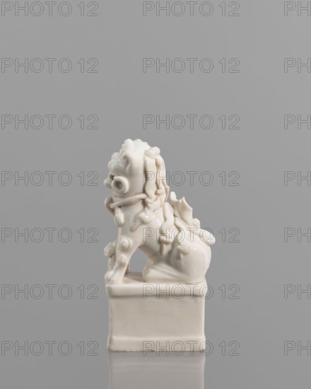 Incense burner in the shape of a fo lion with a ball, lion iconography, fo iconography, ceramics, Chinese art, Chinese culture, censers, animal figurines, incense stands, 18th century, China, sculpture; height 13.0 cm, width 6.0 cm, depth 4.8 cm, A small glossy sculpture of a stylized lion-like creature sits on a rectangular base against a smooth gray background; the sculpture and base are off-white and show flowing, curving carved details like curled mane elements, rounded facial features, coiled decorative motifs along the body, and a curled tail, with subtle shadows and highlights emphasizing the glossy surface.