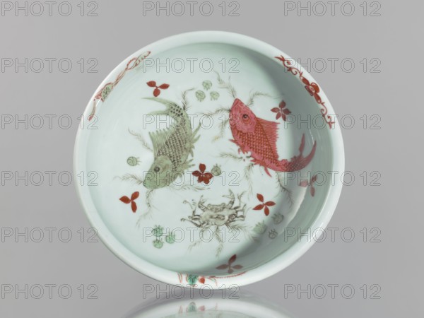 Bowl on an openwork foot;, Chinese, Qing dynasty, Yongzheng period 1723–1735; colored porcelain; decorative vessel depicting fish, carps, and crabs; vessel height 9.5 cm, diameter 23.8 cm; China., A shallow round dish with a pale bluish-white interior decorated with a pair of stylized fish and aquatic motifs; one fish is rendered in a muted green and the other in a reddish-pink, both showing detailed scales and fins. Around them are small floral or leaf-like motifs in red and pale green, and there is a central crab-like creature drawn in light greenish-brown. The rim of the dish has intermittent red decorative accents and the overall background is a soft bluish-white.