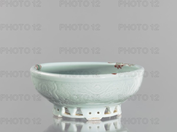 Bowl on an openwork foot; Chinese colored porcelain decorative vessel depicting fish, carps, and crabs; Qing dynasty, Yongzheng period 1723–1735; China; height 9.5 cm, diameter 23.8 cm., A shallow ceramic bowl on a low pedestal foot, shown against a pale gray background, with a glossy celadon glaze in light green and pale blue tones; the bowl exterior has subtle raised decorative patterns in the same light green shade, and the rim shows small accents of reddish-brown; the pedestal foot has open cutouts and areas where the glaze is thinner, revealing warm beige spots, and the bowl casts a soft reflection on the shiny surface beneath.