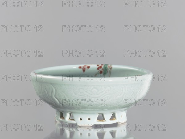 Bowl on an openwork foot;, Chinese colored porcelain vessel from the Qing dynasty, Yongzheng period 1723–1735. Decorative bowl featuring fish carps and crabs. Height 9.5 cm, diameter 23.8 cm., A shallow ceramic bowl with a pale green glaze sits on a reflected surface, showing a rounded rim and a slightly concave interior; the exterior has a subtle raised pattern in the same pale green, while the interior shows a small painted motif in red and green near the rim; the bowl stands on a pierced foot rim with small openings and unglazed edges that reveal a light beige clay, and the overall color palette includes pale green, red, green, beige, and gray from the background and reflection.