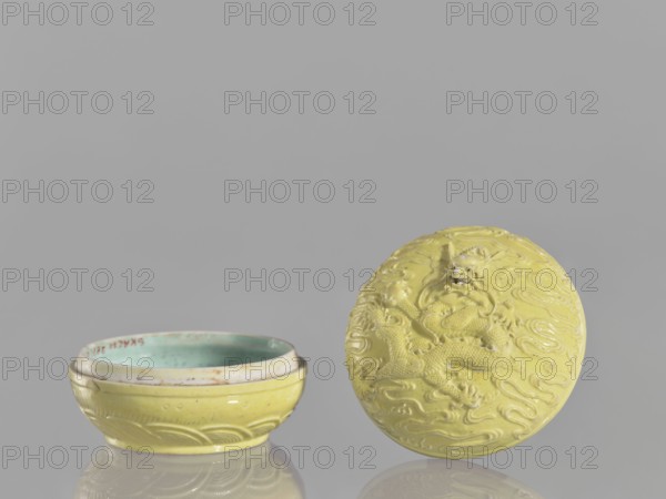 Box with a lid, Kangxi style, ceramics, boxes, Qing style, dragons iconography, Chinese art, Chinese culture, pearls, clouds, Qing 1644–1911, Kangxi 1662–1722, 18th century, China, vessel, height 5 cm, diameter 7.4 cm, A shallow round bowl and its separate lid sit on a reflective surface against a plain gray background; both pieces are primarily yellow with a glossy finish, the bowl interior showing a greenish-blue glaze, and the lid displaying a raised dragon design with flowing cloud-like patterns in the same yellow tone.