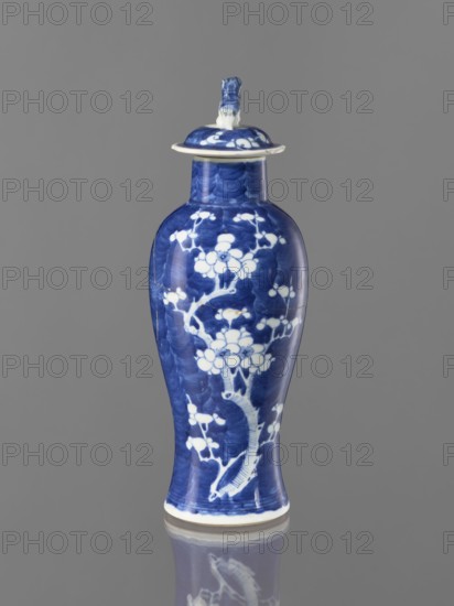 Meiping vase with cover, meiping vessel type, cover, blue and white porcelain, China, 17th–18th century, height 31 cm; decorated with plum trees and floral tendril motifs; ceramics., A tall ceramic vase with a lid stands against a plain gray background, the vase primarily displaying deep blue and white colors with a glossy finish; its surface features floral and branch motifs in white set against the blue, and the lid has a small sculpted handle in the same blue and white.