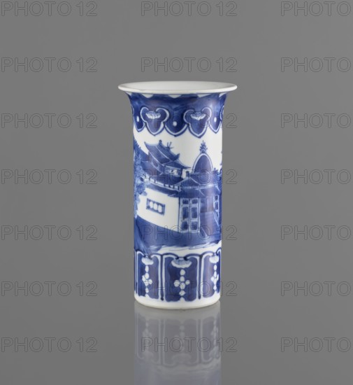 Flute-type vase, blue-and-white porcelain, Chinese, Kangxi period 1662–1722, 17th–18th century. Decorated with landscape motifs. Vessel; height 15 cm, diameter 8.1 cm., A tall cylindrical porcelain vase with a flared rim stands upright against a solid gray background, decorated in blue and white; the upper band features a repeating scalloped motif in deep blue, the central body shows a painted architectural scene with roofs, doorways, and walls rendered in varying shades of blue, and the lower band displays vertical panels with floral-like patterns in blue; the vase sits on a reflective surface that creates a faint mirrored image of its base, and visible colors include blue, white, and gray.