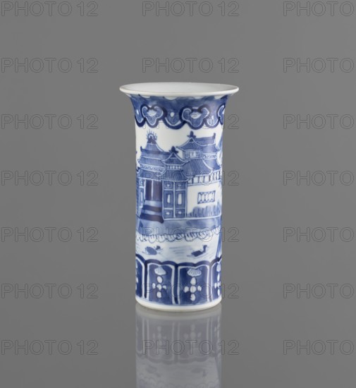 Flute-type vase, ceramics, blue-and-white porcelain, Chinese art, landscape motifs, Chinese, 17th–18th century, China, vessel, height 15 cm, diameter 8.1 cm, A cylindrical ceramic vase with a flared rim standing on a reflective surface, decorated in blue and white; the upper band features a scalloped cloud-like motif in deep blue, the main body shows a painted scene of traditional roofed buildings and architectural details in varying shades of blue, and the lower band displays a repeating floral or petal pattern in dark blue panels; the background and reflection are gray, and the vase has white areas where the base material shows through.