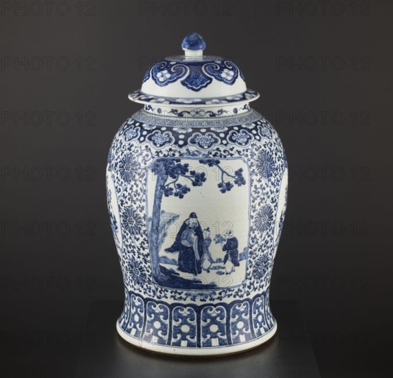 Pot with cover, blue-and-white porcelain, plant motifs and mountain landscapes, decorative vessel, Qing and Ming stylistic influences, possibly 1st half of the 17th century, China; vessel, height 60 cm, diameter 36 cm., A lidded ceramic jar displayed against a dark background, predominantly white with blue painted decoration; the lid has blue floral and scroll motifs and a blue-tipped finial, the shoulder and body are covered with intricate blue floral and scroll borders, and a central rectangular panel on the body shows a blue-painted scene of three human figures beneath a tree; the base area features a repeating blue scroll-and-petal band, and the overall color palette includes shades of cobalt blue and white with a dark backdrop.