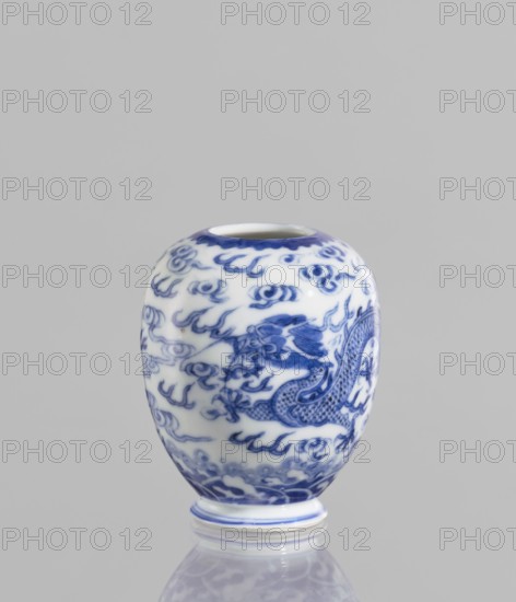 Vase, ceramics, blue and white porcelain, phoenixes, dragons, clouds; Chinese; Qianlong style; 19th century ; China; vessel; height 7.5 cm; diameter 2.5 cm., A small rounded ceramic vase with a glossy white base and intricate blue painted designs, showing a group of swirling cloud-like motifs and a stylized dragon wrapping around the body; the rim and foot have blue accents, and the vase sits on a reflective surface that mirrors its blue and white colors against a plain light gray background.