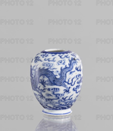 Vase, ceramics, blue and white porcelain, phoenixes, dragons, clouds; Chinese, Qianlong style, 19th century, vessel; height 7.5 cm, diameter 2.5 cm., A rounded ceramic vessel with a glossy white surface decorated in blue, showing a sinuous dragon motif surrounded by stylized cloud-like shapes; the rim and foot have blue accents; the vessel sits on a reflective surface and is set against a plain light gray background.
