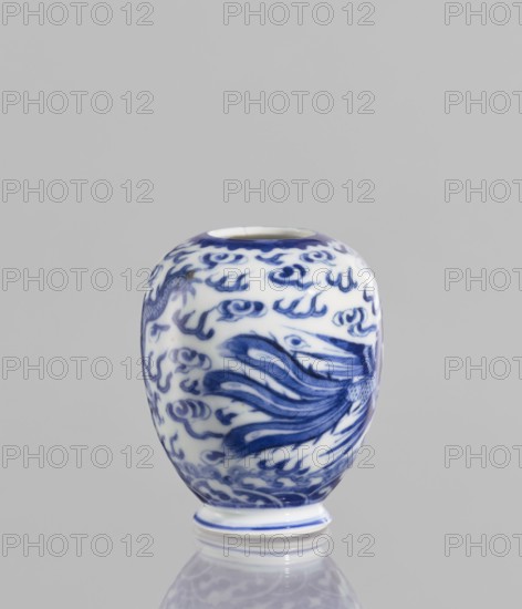 Vase, ceramics, blue and white porcelain, decorated with phoenixes, dragons and clouds; Chinese, Qianlong style, 19th century, China; vessel; height 7.5 cm, diameter 2.5 cm., A small rounded ceramic vessel sits on a reflective surface against a plain light gray background, the vessel glazed in white with an intricate blue painted design of flowing, wave-like motifs and curling cloud-like shapes covering its curved body, a few darker blue brushstrokes suggesting feathery or fin-like forms, a narrow circular opening at the top rim edged in blue, and a short foot with a blue band at the base; visible colors include white, various shades of blue, gray, and a hint of darker navy.