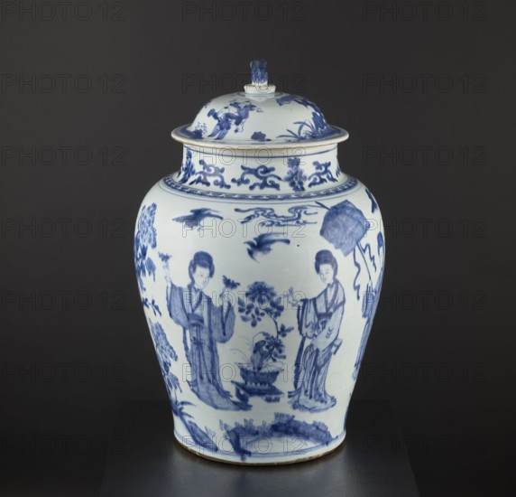 Pot with a cover, Chinese, Qing dynasty 1644–1911, 18th century, blue and white porcelain storage vessel decorated with figurative scenes and images of birds; possibly a Japanese product exported to Europe imitating Chinese wares. Height 58.5 cm, diameter 37 cm., The image shows a lidded ceramic vase with blue painted designs on a white background, placed against a dark gray backdrop and sitting on a dark surface. The vase has a rounded body that tapers toward the base and a flared neck with a lid topped by a small sculpted finial. The painted decoration features human figures in flowing garments, floral motifs, birds in flight, and ornamental scrolls, all rendered in shades of blue. The visible colors in the image are blue, white, dark gray, and black.
