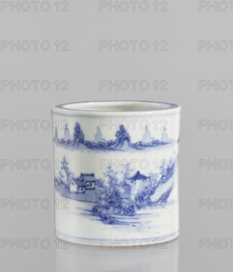 Brush vessel, ceramics, blue and white porcelain, Chinese, 18th century, China; landscape motifs; height 12.8 cm, diameter 12.7 cm; maker, function: brush vessel., A cylindrical ceramic cup sits against a plain light gray background, featuring a glossy white surface decorated with delicate blue painted scenes and decorative bands; the blue imagery includes stylized landscape elements with a few buildings, trees, and flowing forms, and a row of ornamental peaks near the rim, while the rim and base show thin blue outlining.