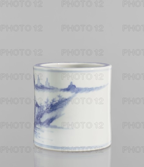Brush vessel, ceramic, blue and white porcelain, Chinese, 18th century, China; decorated with landscape motifs; height 12.8 cm, diameter 12.7 cm., A cylindrical ceramic cup with a glossy white surface sits against a pale gray background, decorated with a delicate blue painted landscape that wraps around its body; the rim and base feature thin blue lines, and the painted scene shows soft blue brushstrokes suggesting distant shapes and textured areas, with the blue varying in intensity from light to deeper tones.