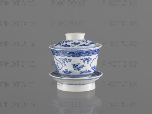 Bowl on a base with a lid, ceramics, blue and white porcelain, Chinese art, female images, figural decorations, Chinese, 19th century, South China, China, vessel, height 8.6 cm, A small porcelain cup with a lid and matching saucer sits against a gray background; the cup and lid are white with intricate blue floral and decorative patterns, and the saucer shares the white base with blue rim detailing; the porcelain has a glossy finish and a subtle reflection is visible on the surface beneath it.