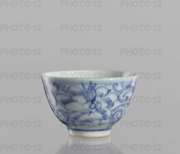 Bowl, blue-and-white porcelain, ceramics, Chinese, 19th century, floral ornament, vessel, height 4.3 cm, diameter 6.7 cm, A small ceramic cup with a rounded shape sits against a neutral gray background, showing a smooth pale off-white interior and exterior decorated with delicate blue floral and scroll patterns. The cup has a slightly flared rim, a narrow foot, and a glossy finish that reflects light. Visible colors include shades of blue, off-white, pale cream around the foot, and gray from the background and reflections.