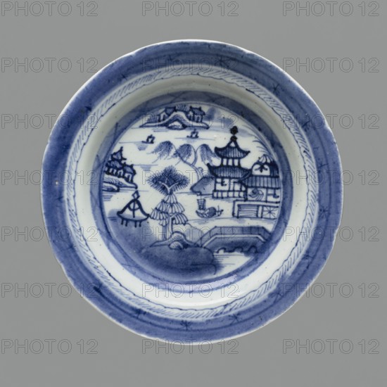 Plate, ceramics, pagoda, blue-and-white porcelain, Chinese art, landscape motifs, 19th century, South China, China; vessel; height 3.5 cm; diameter 22.4 cm., A round ceramic plate with blue and white decoration sits against a gray background. The plate shows a central circular scene painted in blue with stylized landscapes, including a group of pagoda-like buildings, a curved bridge, a tree with layered foliage, and a few small boats on a water area. The rim features concentric bands with decorative brushwork in blue and lighter blue tones, and the plate surface shows some darker blue shading and speckling. The visible colors are blue, white, and gray.