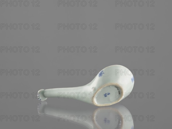 Sauce boat spoon, Chinese, blue-and-white porcelain with plant ornament decoration, tableware element, vessel; Qing dynasty mid-19th century, China; length 19.2 cm., A pale celadon ceramic spoon rests on a reflective surface, showing a smooth curved bowl and a long handle ending in a rounded, slightly flared tip with small blue painted accents; the spoon has small blue floral-like motifs on the exterior of the bowl and a rim with a slightly darker edge, and the reflection beneath mirrors the spoon against a neutral gray background with shades of light and medium gray visible.
