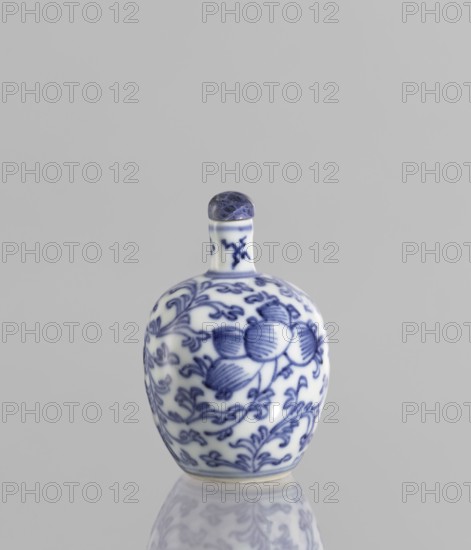 Snuffbox with spoon, Chinese blue-and-white porcelain, 19th century China; decorated with plant ornaments, flowers, and floral tendrils; vessel, height 6.8 cm., A small rounded porcelain bottle with a short neck and rounded stopper sits against a plain light gray background, the bottle decorated with intricate blue floral and vine patterns on a white surface, the stopper appearing darker bluish with marbled texture, and a soft reflection of the bottle visible on the glossy surface beneath.