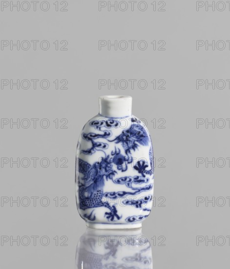 Flask-snuffbox, Chinese; blue-and-white porcelain; ceramics; pearls; clouds; dragons iconography; Kangxi style; Qing dynasty 1644–1911; 19th century; vessel; height 7 cm; ., A small white porcelain bottle with blue painted decorative patterns sits upright against a light gray background; the bottle has a short neck and rounded rectangular body decorated with intricate blue motifs including swirling cloud-like shapes and what appear to be stylized animal or mythical figures, and its glossy surface creates a soft reflection of the same blue-and-white design on the smooth surface beneath it.