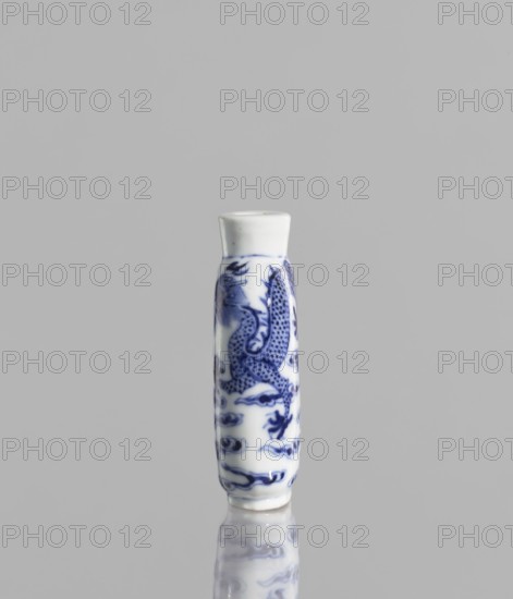 Flask - snuffbox, Chinese, blue-and-white porcelain with pearls and cloud and dragon decoration, Kangxi style Qing dynasty, 1644–1911, 19th century, vessel, height 7 cm, ., A small cylindrical porcelain object stands upright on a reflective surface, decorated with a blue painted dragon motif and swirling cloud-like patterns on a white background, with a plain white rim at the top; the scene shows shades of blue, white, gray, and a touch of darker blue in the reflected area.
