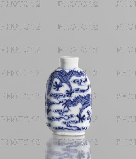Flask - snuffbox, Chinese, blue-and-white porcelain, pearls, clouds, dragons iconography, Kangxi style, Qing 1644–1911, 19th century, China, vessel, height 7 cm, ceramics., A small porcelain bottle stands upright against a plain gray background, predominantly white with blue painted decorative patterns; the bottle has a rounded rectangular body and a short cylindrical neck, with blue sinuous dragon-like motifs and swirling cloud-like designs wrapping around its surface, and its glossy finish creates a soft reflection of the bottle on the surface below.