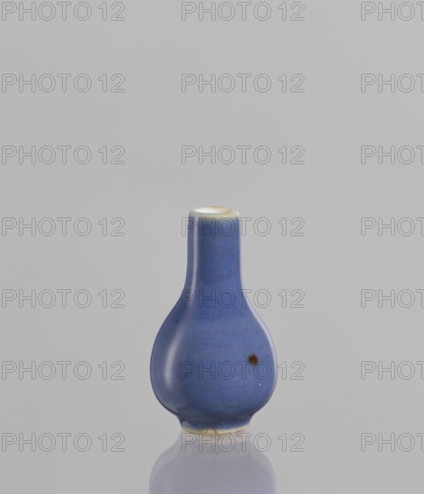 Bottle, Chinese, Chinese art, ceramics, poudre bleu, 19th century, China, vessel, height 5.3 cm, A small rounded vessel with a narrow neck and bulbous body sits centered against a pale gray background, the vessel glazed in a smooth blue with a few small darker spots and a darker circular blemish on one side, the rim showing a thin band of off-white and a hint of pale yellow, and the base revealing an unglazed rough area in a beige tone; the surface has a soft sheen and its reflection is visible on the glossy surface beneath.