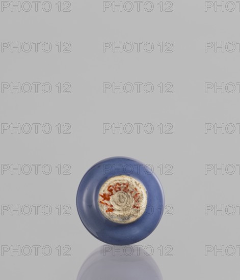 Bottle, Chinese, ceramics, poudre bleu, 19th century, China, vessel, height 5.3 cm, A single round object with a smooth blue outer surface sits near the bottom center of the image against a light gray background, showing a worn circular central area with a rougher texture and patches of reddish and beige tones; a subtle reflection of the object appears beneath it on the surface.