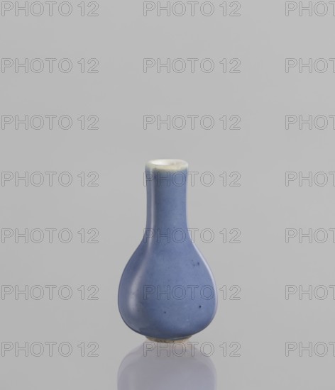 Bottle, Chinese, 19th century, ceramics, blue and white porcelain poudre bleu, vessel, height 5.3 cm, A small teardrop-shaped ceramic vessel with a narrow cylindrical neck and rounded body sits upright on a reflective surface; the vessel is glazed in a soft matte blue with subtle darker speckles and a slightly lighter rim that shows a pale off-white edge, and the background is a smooth neutral light gray.