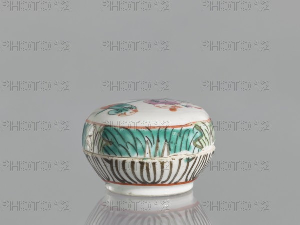 Box with a lid, Chinese, Chinese art, figural scenes, colored porcelain, boxes, 19th century, China, vessel, height 4.6 cm, width 6.9 cm, A small round ceramic box with a lid sits on a reflective surface against a gray background; the box is primarily white with decorative bands of turquoise, black, green, pink, orange, and brown, featuring a painted floral or leaf motif around the sides and a partially visible painted design on the lid, with thin orange edging and a glossy finish.