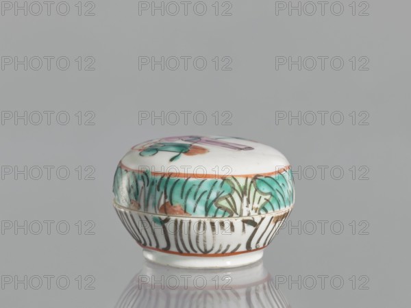 Box with a lid, Chinese, 19th century, colored porcelain box with figural scenes, vessel, height 4.6 cm, width 6.9 cm, A small round ceramic box with a domed lid sitting on a reflective surface, decorated with painted floral and foliage motifs; the top and sides show teal green, coral orange, pale pink, black, and white colors, with the white forming the base and background and the other colors used for stylized leaves, petals, and linear accents.