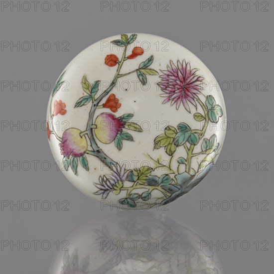Lidded box, Chinese, colored porcelain decorated with pomegranates, chrysanthemums and peonies in floral ornament; mid-19th century Qing dynasty, 1644–1911; vessel used for writing instruments; height 3.2 cm, diameter 7.9 cm., A round ceramic object with a glossy white surface decorated with a painted botanical scene featuring a branch with leaves and blossoms in shades of green, teal, and yellow, flowers and fruit in pink, magenta, and pale purple, and small accents in orange and red, all set against a neutral gray background with a soft reflection of the object below.