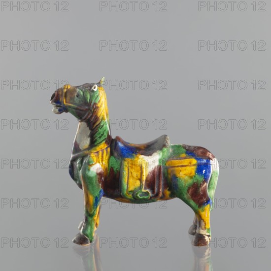 Mule, Chinese, Qing dynasty 1644–1911, 18th century. Colored porcelain animal figurine mule, sculpture. Height 19.1 cm; width 19.4 cm., A small glazed ceramic figure of a horse shown in profile against a plain gray background, with a glossy surface displaying a mix of green, yellow, blue, brown, and white colors, a raised saddle area, a stylized mane and tail, defined legs and hooves, and a slightly open mouth and visible eye, with the figure casting a faint reflection below.
