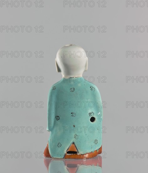 Boy with ruyi — incense burner; maker, Chinese; colored porcelain; 19th century; ruyi scepter iconography; depicts a boy child; sculpture; height 15 cm., A small ceramic figure shown from the back with a smooth white head and ears, wearing a turquoise-green robe decorated with several small simple floral motifs, and a rusty orange base visible at the hem; there is a round hole on one side of the robe and a triangular cutout at the lower center, all set against a plain light gray background.
