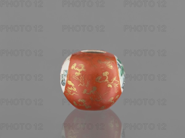 Vase, Chinese, Qing 1644–1911, early 19th century. Porcelain jug/vessel with birds, female images, and landscape motifs. Height 7.4 cm; diameter 8.6 cm., A round ceramic vessel sits against a neutral gray background, showing a smooth glossy surface with a dominant reddish-orange band around its middle decorated with shiny gold motifs, flanked by white vertical panels that contain painted scenes in green, blue, and black. The vessel's rim is a pale off-white, and the base reflects faintly on the glossy surface beneath it. The visible colors include reddish-orange, gold, white, green, blue, black, pale off-white, and gray.