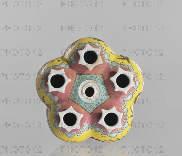 Vase in the shape of five connected vases on a base, Chinese, colored porcelain, dragons and floral decorations, ceramics, 18th/19th century, China, vessel, height 15.8 cm, A flower-shaped ceramic object with a scalloped yellow outer edge and a central area of pink and turquoise; it has a patterned turquoise pentagonal section at the center and a ringed circular opening in the middle, surrounded by a group of five star-shaped white-rimmed openings arranged around the center. The surface shows decorative cloud-like motifs in turquoise and brown, with some darker brown brush-like marks on the yellow areas. The background is a plain light gray, and the object rests on a reflective surface that creates a subtle mirrored reflection. Colors visible include yellow, pink, turquoise, white, brown, black, and gray.