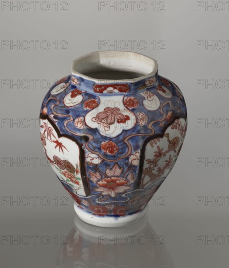 Vase with cover, Japanese, Edo period 1603–1868, 18th century; ceramics Imari; decorated with flowers, tree, bamboos, peonies, and karashishi iconography; vessel; height 25.5 cm, diameter 16 cm., A rounded ceramic vase with a slightly flared and octagonal rim sits against a neutral gray background, decorated with a complex painted pattern in blue, red, white, and touches of green and brown; the body shows cloud-like white panels outlined in dark blue and red, filled with floral motifs and stylized blossoms in red and pink, set against a deep blue ground with swirling lines and small floral accents, and the lower section features a large lotus-like flower in red and pink.