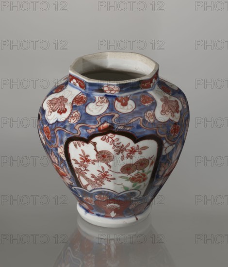 Vase with cover, Japanese, Edo period 18th century, imari ceramics decorated with flowers, tree, bamboos, peonies, and karashishi; vessel, height 25.5 cm, diameter 16 cm., A glazed ceramic vase with a rounded body and a slightly flared, irregular rim sits on a reflective surface; its overall palette includes blue, white, red, green, and brown tones, with blue forming a background of flowing patterns and white panels framed in dark brown displaying floral and circular motifs in red and green; the vase surface is covered with decorative cloud- and flower-like shapes in red and blue, and the interior visible at the top appears off-white to light beige.