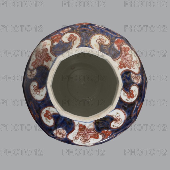Vase with cover, Japanese, Edo period 1603–1868, 18th century, imari porcelain vessel decorated with flowers, tree, bamboos, peonies, and karashishi; height 25.5 cm, diameter 16 cm., A top-down view of a round ceramic vessel with a wide octagonal opening, showing a smooth gray interior and a patterned rim decorated with swirling blue and white panels and floral motifs in red and gold accents, set against a plain light gray background.