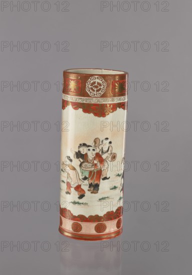 Vase, Kutani; porcelain; cylindrical vessel depicting one hundred sons boys in figurative scenes with plant ornaments; Japanese; 1868–1912; height 30 cm, diameter 12 cm., A tall cylindrical ceramic vase standing against a plain gray background with a reflective surface at the base; the vase has a predominantly cream-colored body with crackle glaze and decorative red bands at the top and bottom featuring gold accents; a painted scene of a group of children in traditional clothing wraps around the middle, showing garments in red, green, black, and white with small patches of pink and beige, and small areas of green indicating grass; the top band includes ornate circular and floral motifs in red and gold, and the lower band has repeating circular designs in red and gold.