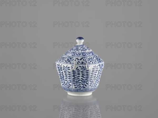 Sugar bowl with lid, ceramics, sugar bowl, Chinese art, Chinese culture, lid, 20th century, China, vessel, height 12 cm, A small lidded ceramic vessel sits centered against a plain grey background, showing a white base color with intricate blue painted floral and geometric patterns covering the body and domed lid; the lid has a rounded knob topped with a blue band, and the vessel has a small curved handle on one side; the object and its patterned reflection are visible on the smooth reflective surface beneath it, with the visible colors being blue, white, and grey.