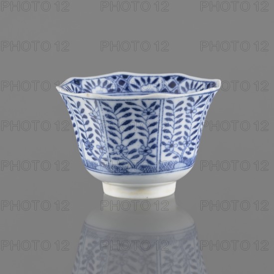 Bowl, Chinese, ceramics, 20th century, China, vessel, height 5.3 cm, diameter 7.8 cm, A small porcelain cup with a flared, scalloped rim sits against a gray background, decorated with a blue floral and leafy pattern on a white surface; the exterior shows vertical panels filled with stylized leaves and flowers in blue, a blue band along the foot, and a slightly raised white base, with a faint reflection of the cup visible on the surface below.