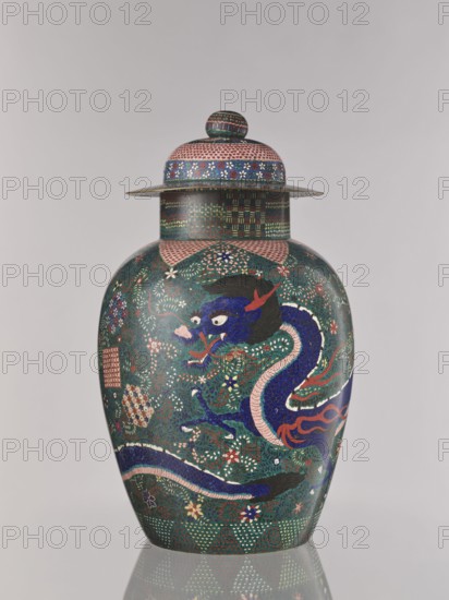 Vase with cover, Japanese, cloisonné enamel, Meiji 1868–1912, Man'en ca. 1860–1870, Japan; vessel with cover decorated with dragons, plant ornament, geometric-plant ornament, shippo pattern, kikko pattern, asanoha pattern; height 57.0 cm., A lidded vase with a rounded body and a flared shoulder sits against a neutral pale background, decorated overall in deep green with intricate patterns in dark blue, pink, red, white, yellow, and black; a prominent sinuous dragon motif in dark blue with pink accents and red flames winds around the body, set among stylized floral and leaf patterns in white, pink, yellow, and red, with small dotted and lattice-like geometric bands in green, pink, and blue near the neck and base, and a domed lid topped by a small round finial carrying matching multicolored patterned bands.