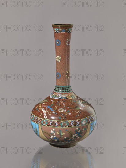 Vase, Japanese, Meiji 1868–1912, ca. 1880 Meiji 13; cloisonné enamel vessel depicting plants, butterflies, phoenixes hoo/kinseki; height 30.5 cm, diameter 16.0 cm., A tall, slender-necked vase with a bulbous base stands against a plain neutral background; the vase has a predominantly reddish-brown surface decorated with a repeating small swirl pattern and scattered floral motifs in blue, white, yellow, green, and gold, a band of turquoise and brown checker detailing near the neck, a wide ornate band around the shoulder with complex floral and vine patterns in blue, turquoise, gold, white, and green, and panels around the lower body featuring stylized flowers and small bird motifs in blue, green, white, yellow, and gold, all resting on a dark base that casts a subtle reflection on the surface below.