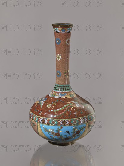 Vase, Japanese art, Japanese culture, plants, butterflies, phoenixes iconography, Meiji 1868–1912, hoo phoenix, cloisonné enamel, ca. 1880 Meiji 13, Japan, vessel; height 30.5 cm, diameter 16.0 cm, A decorative vase with a long narrow neck and rounded body sits against a neutral gray background, showing a base color palette of brown and blue with accents of gold, green, white, red, and black; the neck is predominantly brown with a repeating small swirl pattern and scattered floral motifs in blue, white, green, and red, while the shoulder and body feature ornate floral and foliate designs in turquoise blue panels and reddish-brown areas embellished with gold outlines and green leaves, along with bands of geometric and scalloped patterns in turquoise, black, white, and gold; the vase has a glossy finish that produces highlights and a subtle reflection on the surface beneath it.