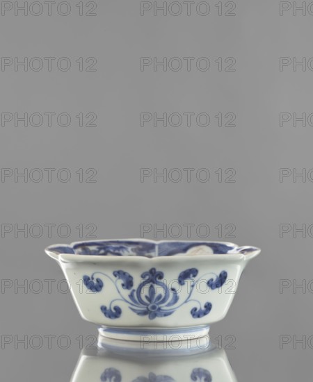 Bowl, ceramics, blue-and-white porcelain, decorated with animals and plant ornaments; maker, period: Chenghua 1465–1487 and Edo 1603–1868 influences; likely 18th century, Arita, Japan; vessel; height 6.0 cm, width 15.0 cm; ., A shallow porcelain bowl with a scalloped rim sits on a reflective surface, showing pale white and blue colors; the exterior features a blue floral and scroll motif painted around its sides, and the interior rim also shows blue decorative patterns; the bowl has a short foot ring with blue bands and the reflection below mirrors the bowl’s shape and decorations.
