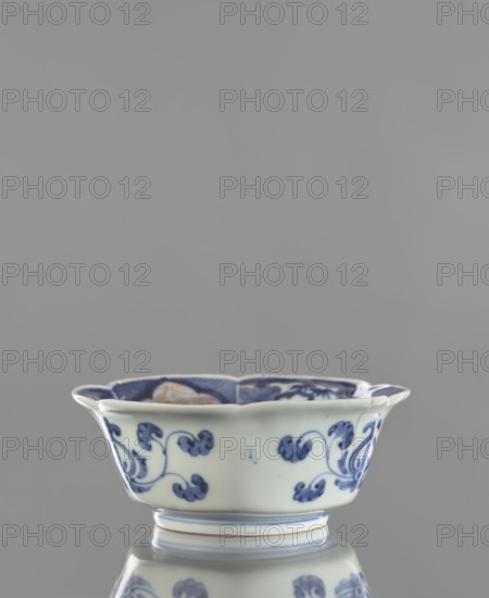 Bowl, ceramics, blue-and-white porcelain, decorated with animals and plant ornaments; bowl-shaped vessel, Japanese, Arita; possible dates: Chenghua 1465–1487, Edo 1603–1868, or 18th century, height 6.0 cm, width 15.0 cm., A shallow ceramic bowl with a scalloped rim sits centered against a solid gray background, showing a white base color decorated with blue floral and scroll motifs on its exterior and inner rim; the bowl rests on a short foot and has a reflective surface beneath that mirrors its blue-and-white pattern.