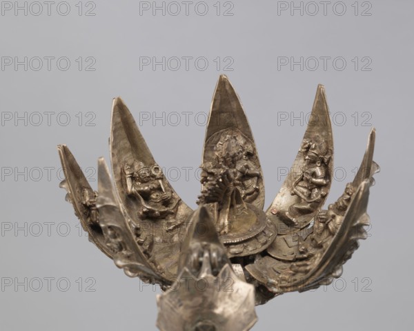 Lotus flower with Buddhist deities, 19th century, Nepal; bronze lotus mandala depicting Hevajra and consort/Nairatmya Buddhist deities, Himalayan/Nepalese Buddhist art; cult object; iconography: lotus, pairs of lovers, bodhisattva, enlightenment; height 20.3 cm, width 8.0 cm., A metallic lotus-like sculpture with several curved petal elements arranged around a central raised platform, each petal featuring small sculpted figurines and ornamental relief work, all rendered in a bronze to brass color range with patinated darker brown and greenish areas, set against a plain light gray background.