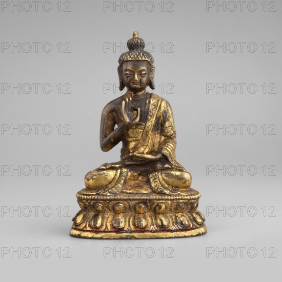Shakyamuni Buddha, Buddha iconography, Himalayan/Tibetan Buddhist art, Buddha ca. 560–480 BCE, ushnisha, 19th century, Tibet, sculpture figurine, height 6.7 cm, width 3.3 cm, depth 4.1 cm, A small seated statue of a figure with a topknot hairstyle, shown in a meditative pose with one hand raised and the other resting in the lap; the figure wears draped robes and sits on an ornate rounded base with repeating petal-like motifs. The surface shows areas of shiny gold and darker aged patina, with hints of reddish tones near the base; the background is a smooth neutral gray.