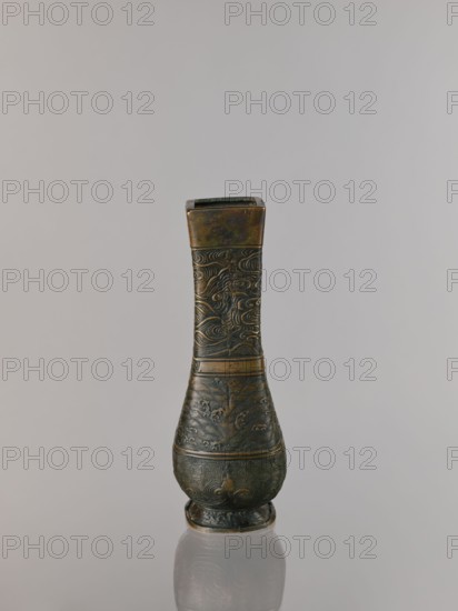 Hu-type vase, relief decoration, hu vessel, Chinese art, Chinese culture, meander ornament, ceremonial vessels, clouds, sea waves, ritual vessels, Xuande 1426–1435, Ming 1368–1644, Qing 1644–1911, backdated signatures, quadrilateral with rounded lower edges. With an inscription. 17th century, China; vessel; height 24.0 cm; width 12.0 cm., An upright narrow vase-like object with a flared square top and a rounded base sits centered against a pale gray background, showing a metallic surface with patinated greenish-bronze and darker brown tones; the body is decorated with carved swirling and wave-like patterns, bands encircling the form, and textured geometric motifs near the lower section, and the object casts a soft reflection on the glossy surface beneath it.